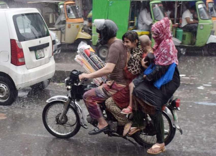 لاہور: ایک موٹر سائیکل سوار فیملی موسلا دھار بارش میں اپنی ..