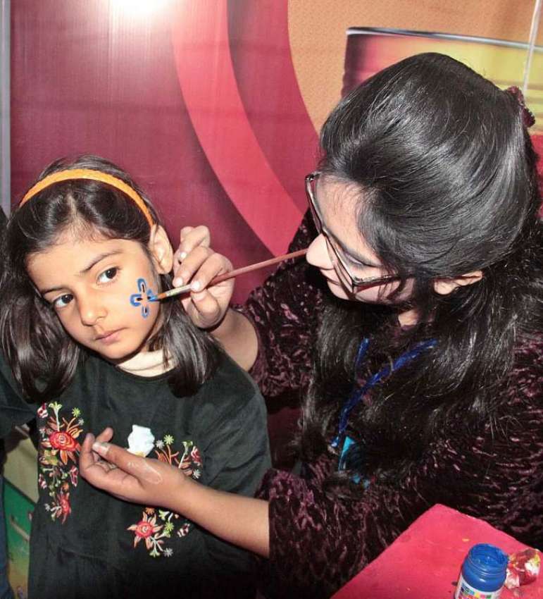لاہور: پینٹنگ مقابلے کے دوران  ایک خاتون بچے کے چہرے پر رنگ ..