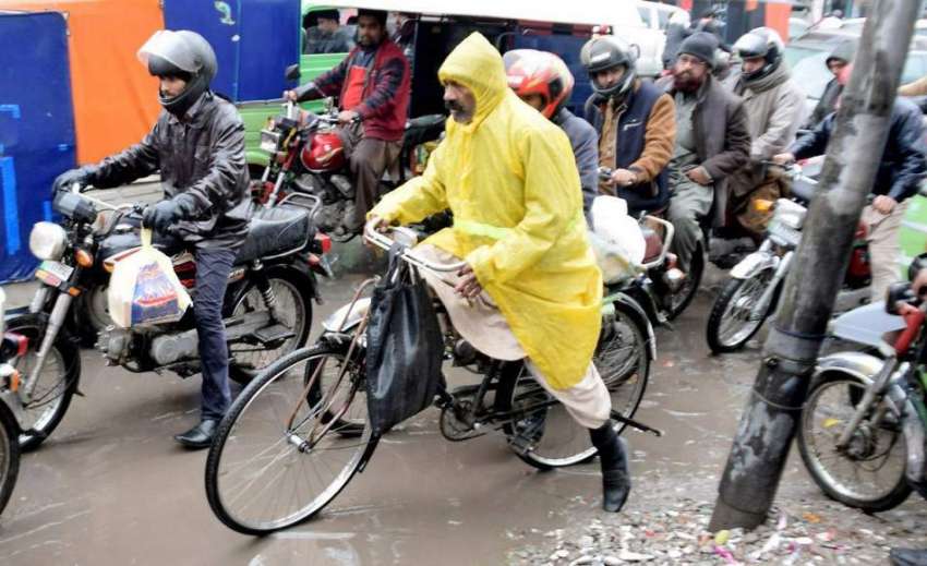 لاہور: ایک سائیکل سوار بارش سے بچنے کے لیے برساتی پہنے جارہا ..