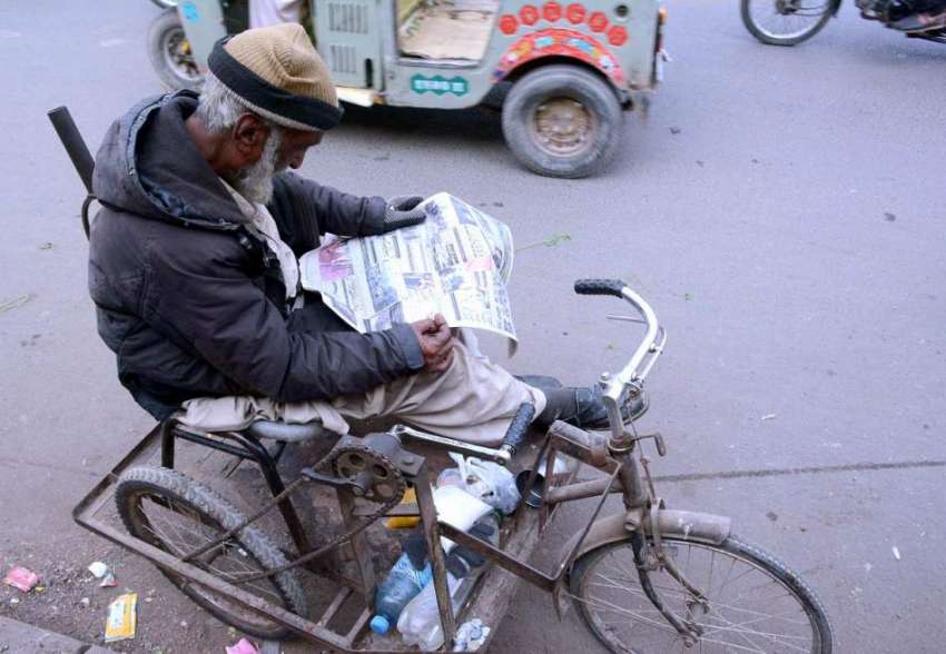 کراچی: معذوری کا شکار شخص سڑک کے کنارے اخبار پڑھ رہا  ہے۔