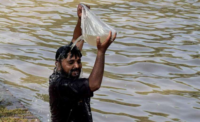 لاہور: ایک شہری نہر کنارے گرمی کی شدت کم کرنے کے لیے اپنے ..