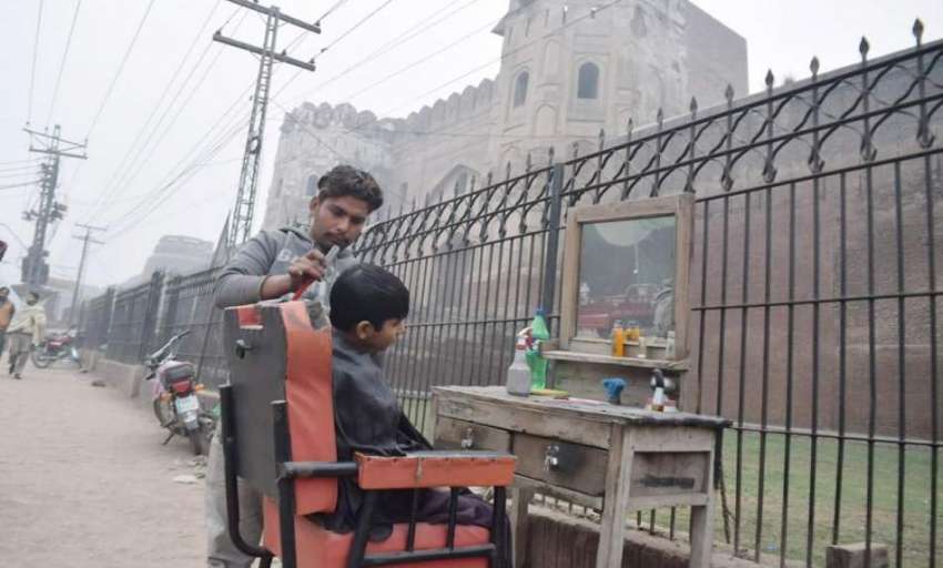 لاہور: ایک حجام شاہی قلعہ کی دیوار کے ساتھ دکان سجائے بچے ..