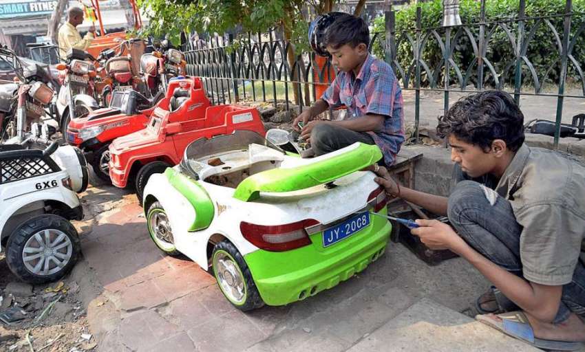 لاہور، کاریگر بچے مقامی دکان پر بچوں کی گاڑیوں کی مرمت کر ..