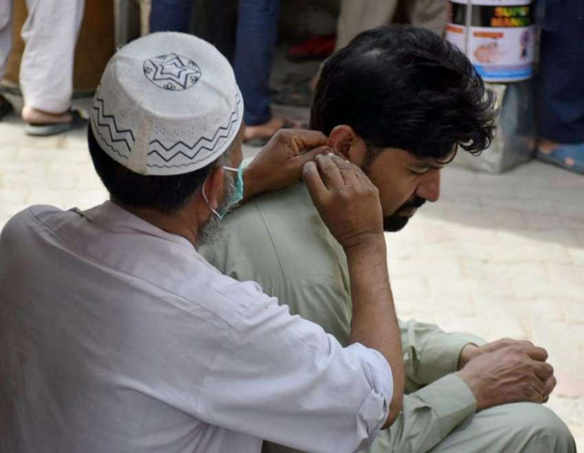 لاہور : ایک شخص سڑک کنارے بیٹھے عطائی سے کان کی صفائی کروار ..