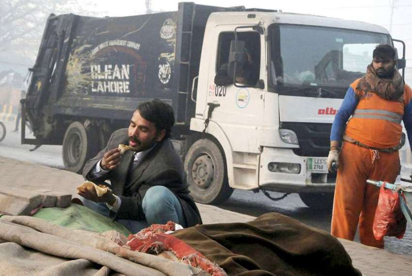 لاہور: ایک شخص کوڑے والی گاڑی کے پاس بیٹھا کھانا کھا رہا ..