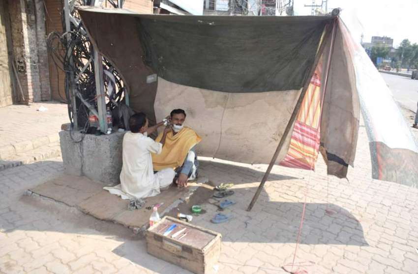 لاہور: ایک حجام سڑک کنارے ترپال لگا کر بنائی گئی دکان میں ..