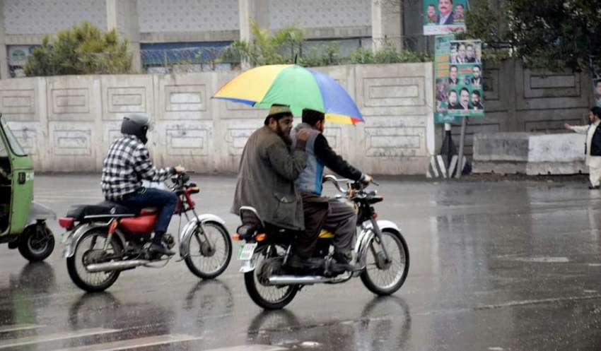 لاہور: بارش سے بچنے کیلئے موٹر سائیکل سوار شہری چھتری تانے ..