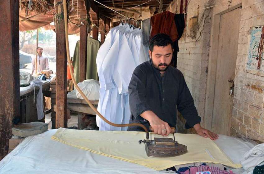 فیصل آباد: دکاندار اپنی دکان میں کپڑے استری کر رہا ہے۔