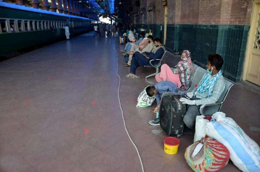 لاہور: ریلوے اسٹیشن پر مسافر ٹرین  کے انتظار میں بیٹھے ہیں۔ ..