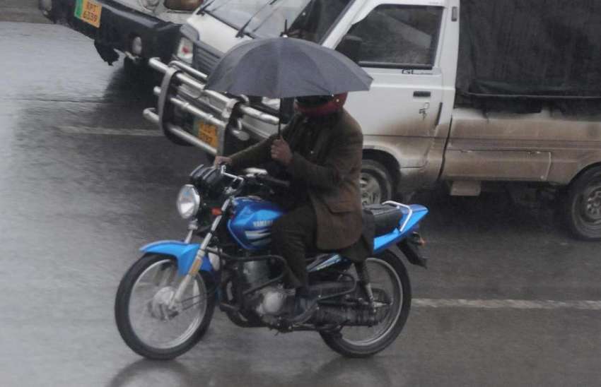 راولپنڈی، بارش کے دوران ایک موٹرسائیکل سوار چھتری تانے ..