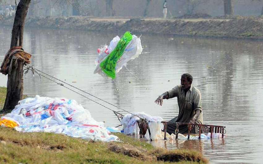 ملتان: مقامی نہر پر مزدور خالی بیگ دھونے کے بعد نہر سے باہر ..