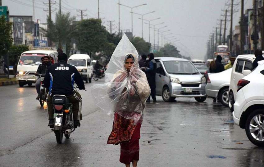 سیالکوٹ: بارش سے بچنے کے لئے ایک خاتون پلاسٹک کی چادر کے ..