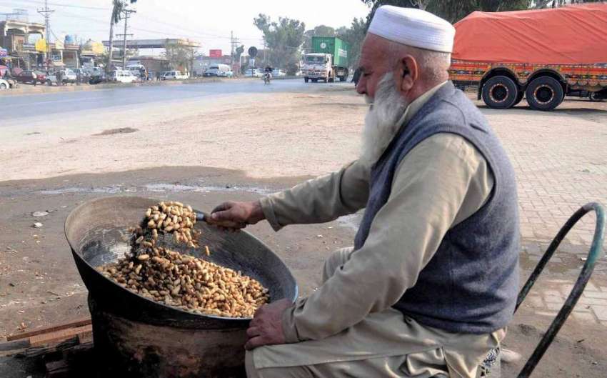 راولپنڈی:ایک معمرشخص سڑک کنارے مونگ پھلی بھوننے میں مصروف ..