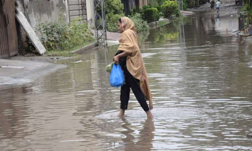 لاہور : ایک خاتون سودا سلف لئے بارش کے کھڑے پانی میں سے گزر ..