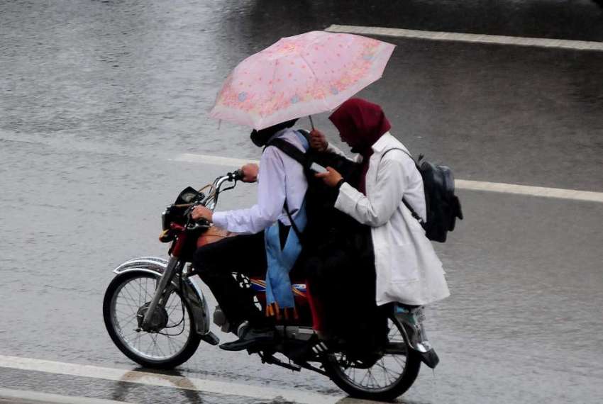 راولپنڈی، بارش کے دوران موٹرسائیکل پر سوار لڑکی بارش سے ..