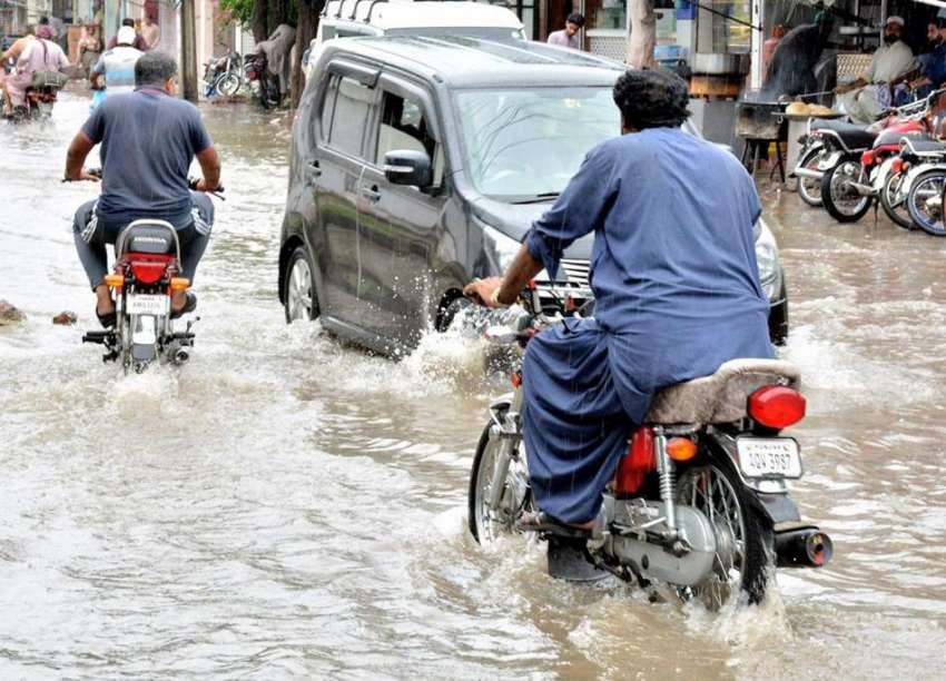 لاہور، بارش کے بعد سڑک پر جمع پانی سے ٹریفک گزر رہی ہے۔